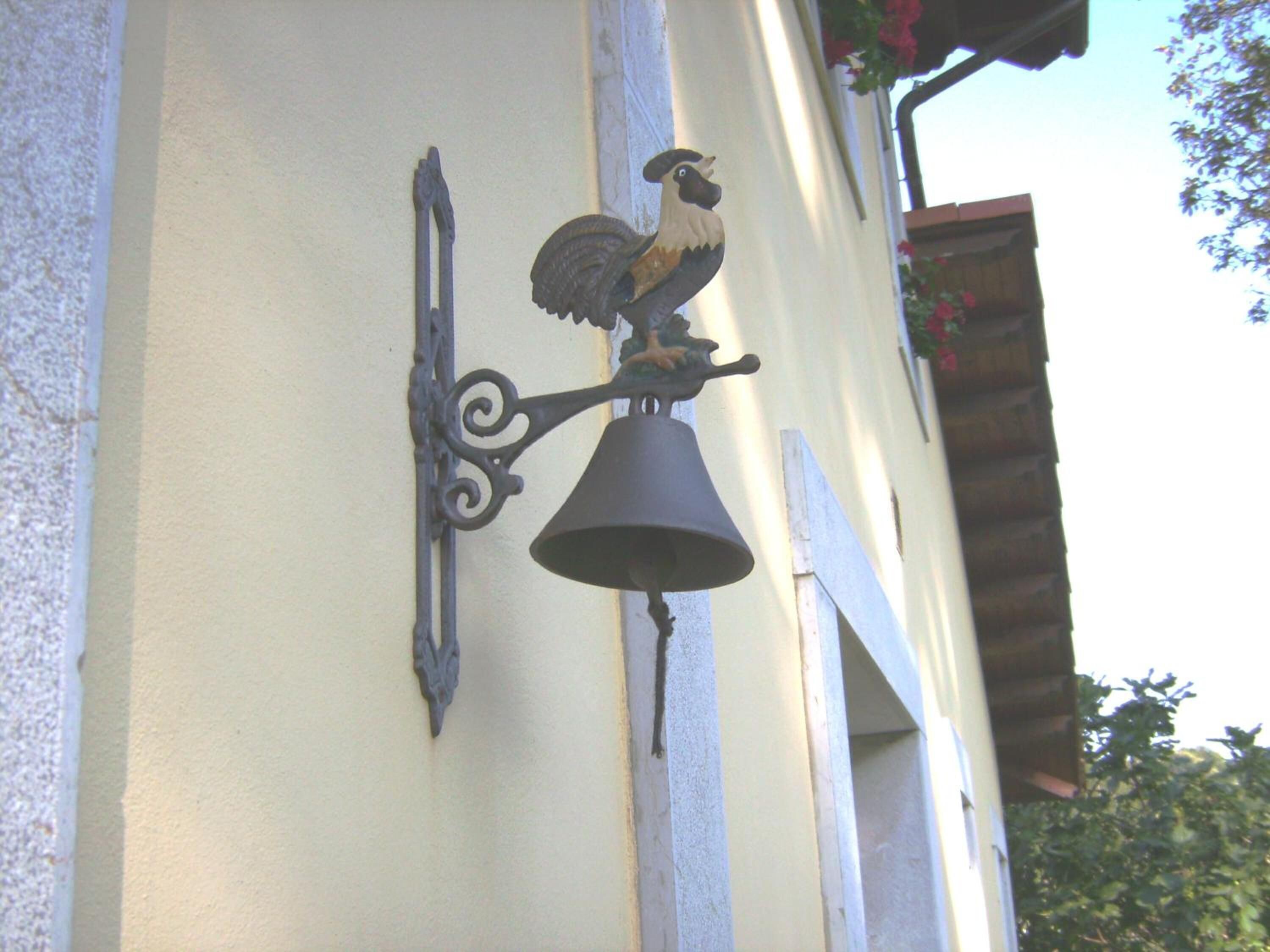 A wall-mounted bell with a rooster figure, attached to a building's exterior.