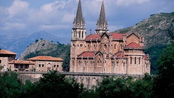 A historic church with two tall spires, surrounded by greenery and mountains.