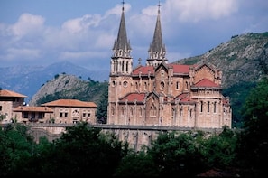 A historic church with two tall spires, surrounded by greenery and mountains. - Casa De Aldea El Frade (Ribadesella)