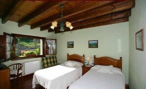 A room with two single beds, a wooden ceiling, and a window with a view of greenery.