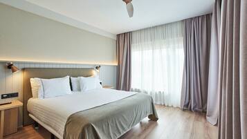 Habitación de hotel con una cama grande, piso de madera, ventilador de techo y ventana con cortinas.