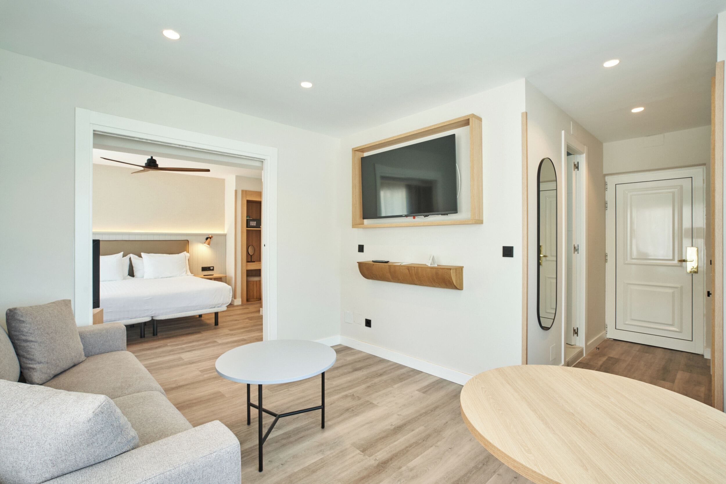 Una habitación de hotel moderna con cama, sofá, mesa redonda, televisor y espejo.