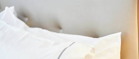 A bed with white bedding and a grey stripe on the pillow.