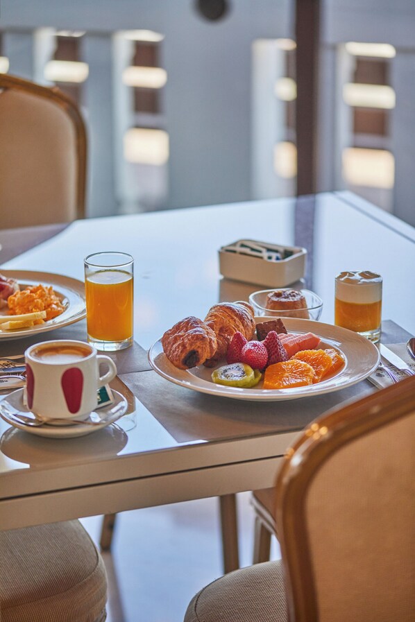 Desayuno con croissants, frutas y bebidas sobre una mesa.