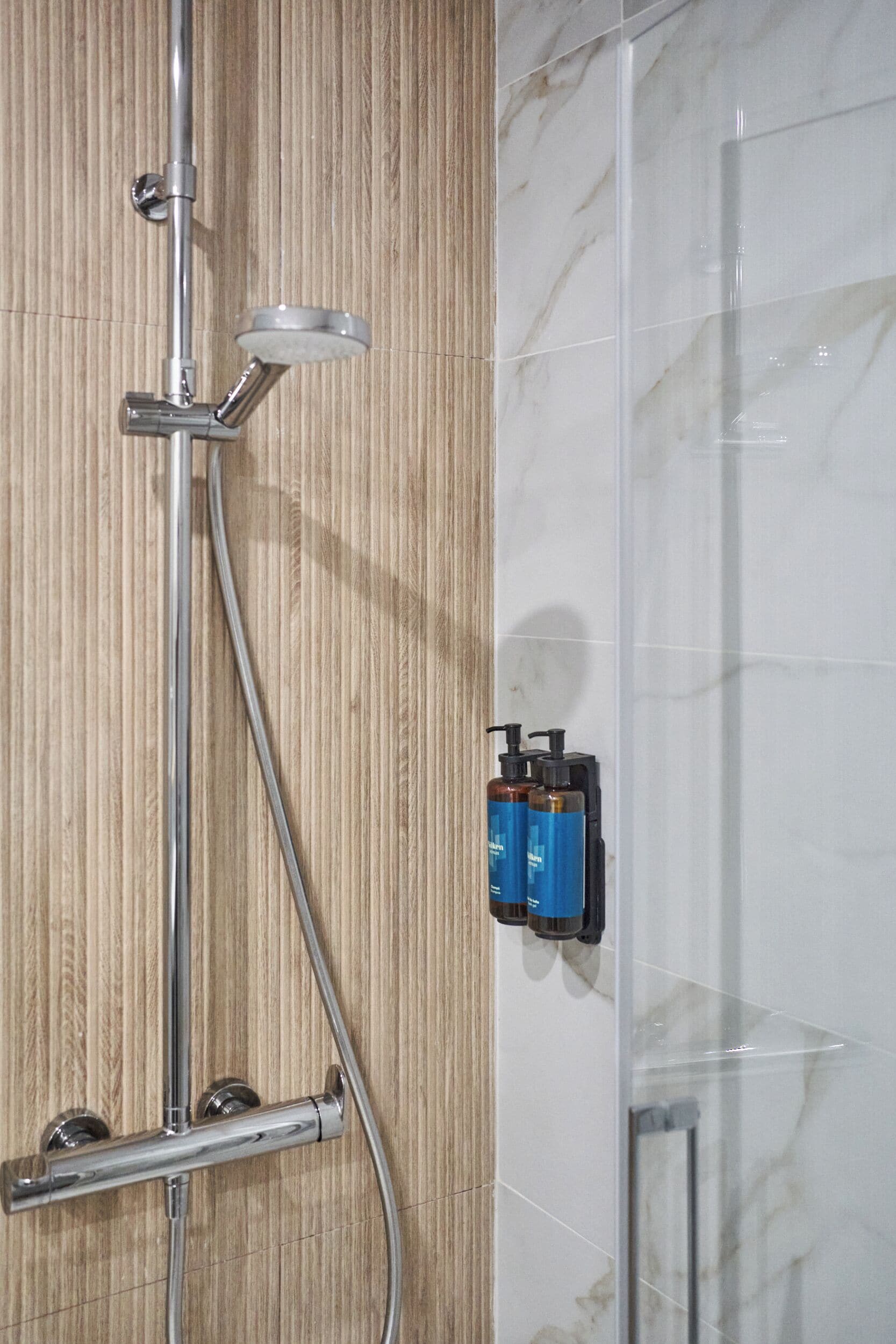 A shower with a handheld showerhead, a wall-mounted control panel, and a glass shower enclosure.