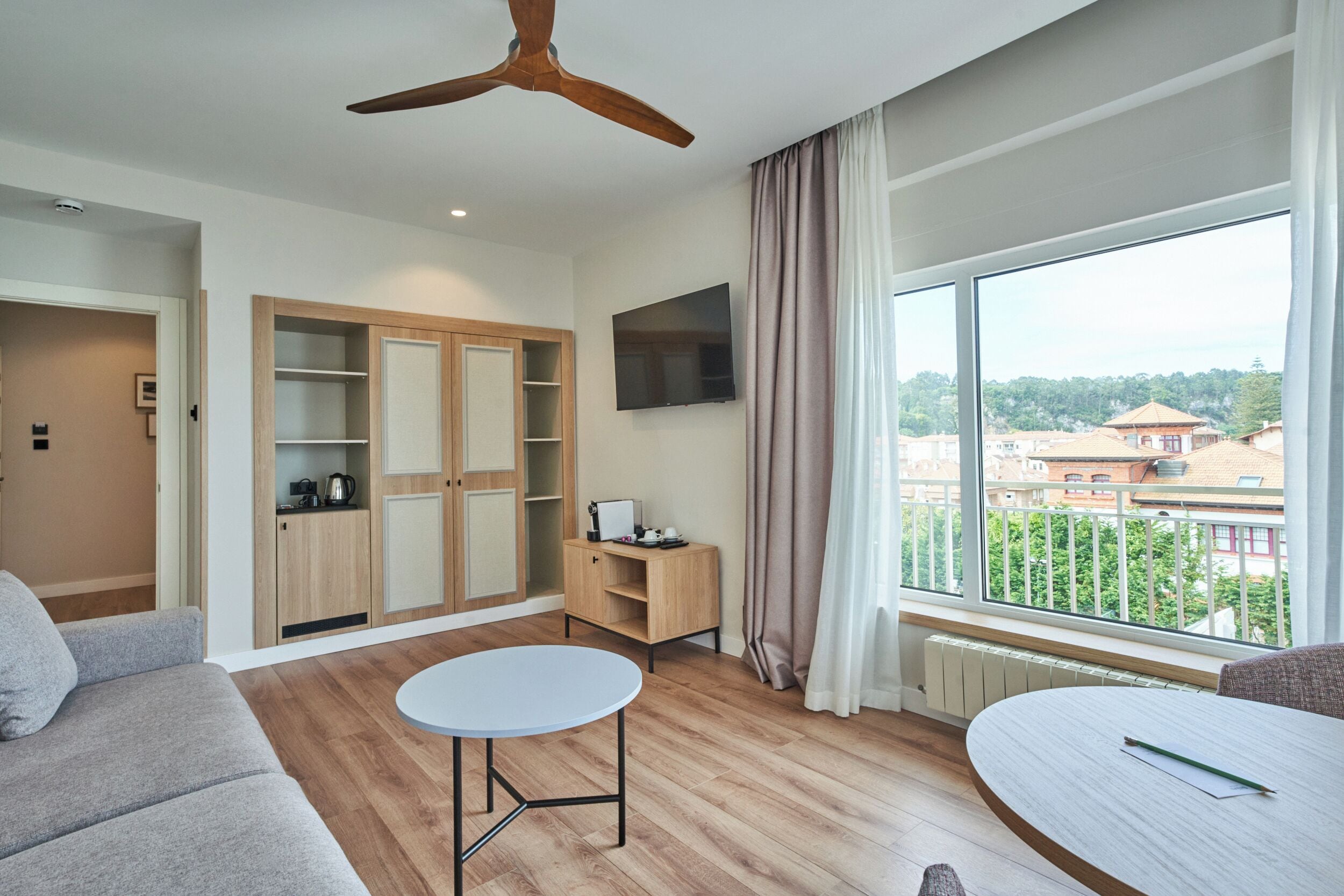 Una sala moderna con ventilador de techo, televisor, un ventanal con vistas, sofá y una pequeña mesa.