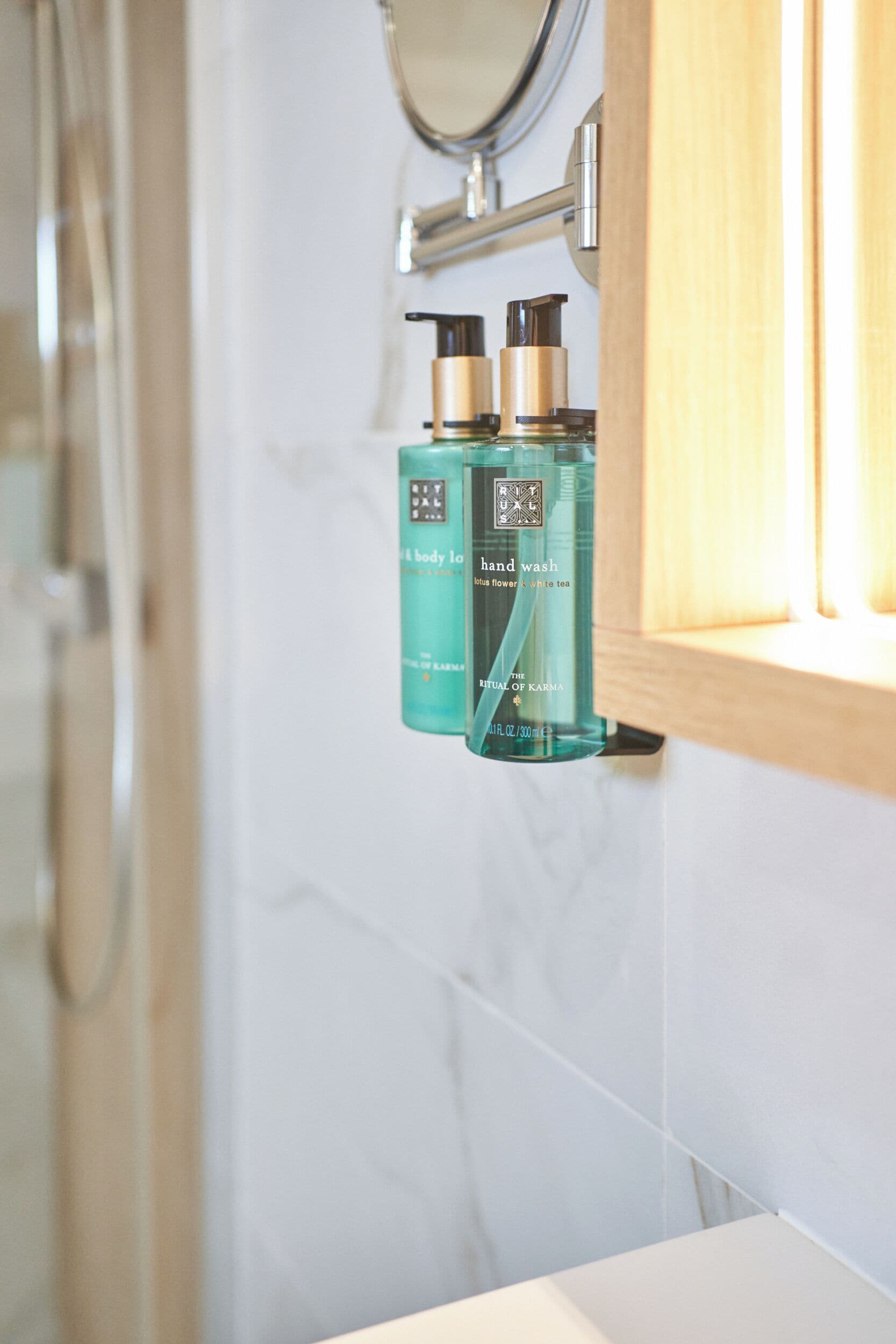 A bathroom with a marble wall, a wooden cabinet, and two bottles of hand wash soap.
