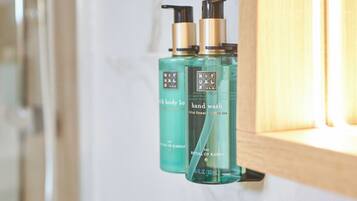 A bathroom with a marble wall, a wooden cabinet, and two bottles of hand wash soap.