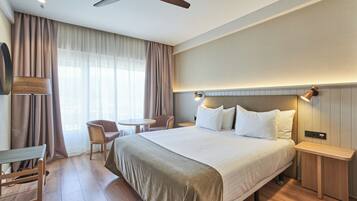 A hotel room with a bed, bedside tables, a chair, a desk, a ceiling fan, and a TV.