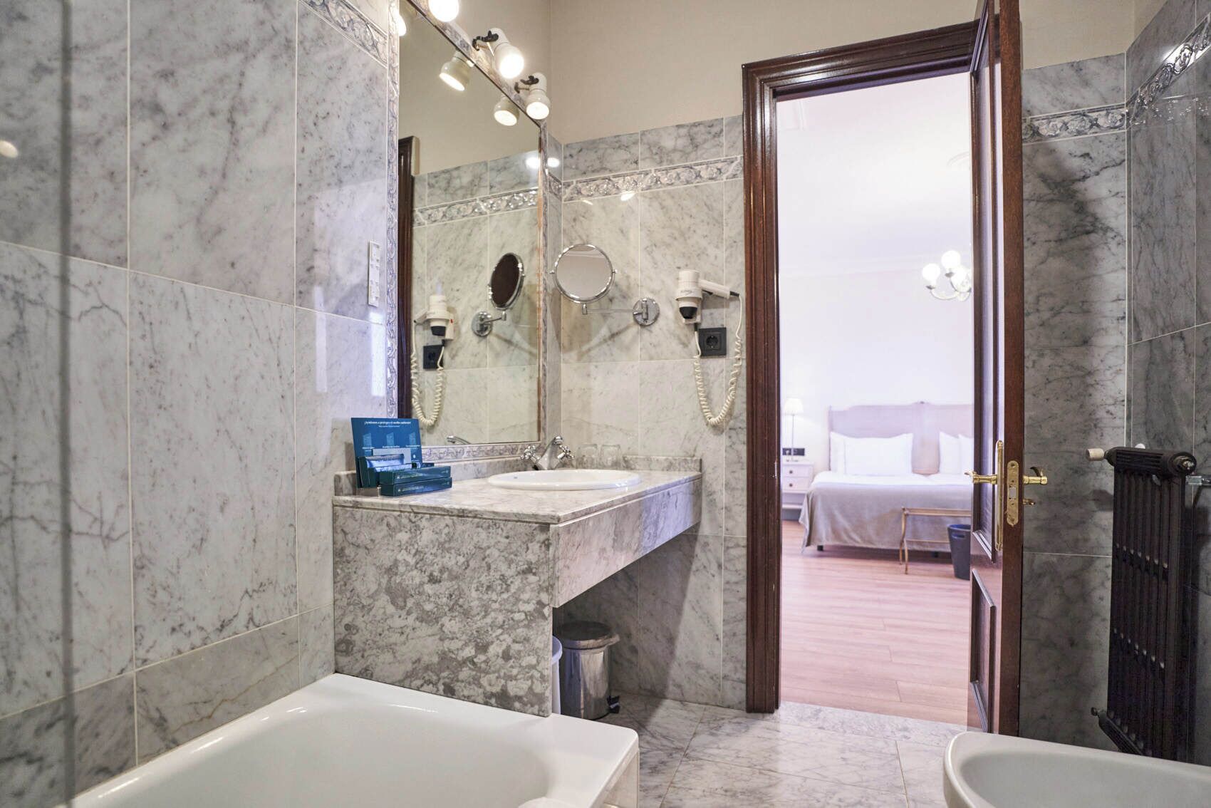 Un baño con lavamanos de mármol, un espejo grande, una bañera y zona de ducha.