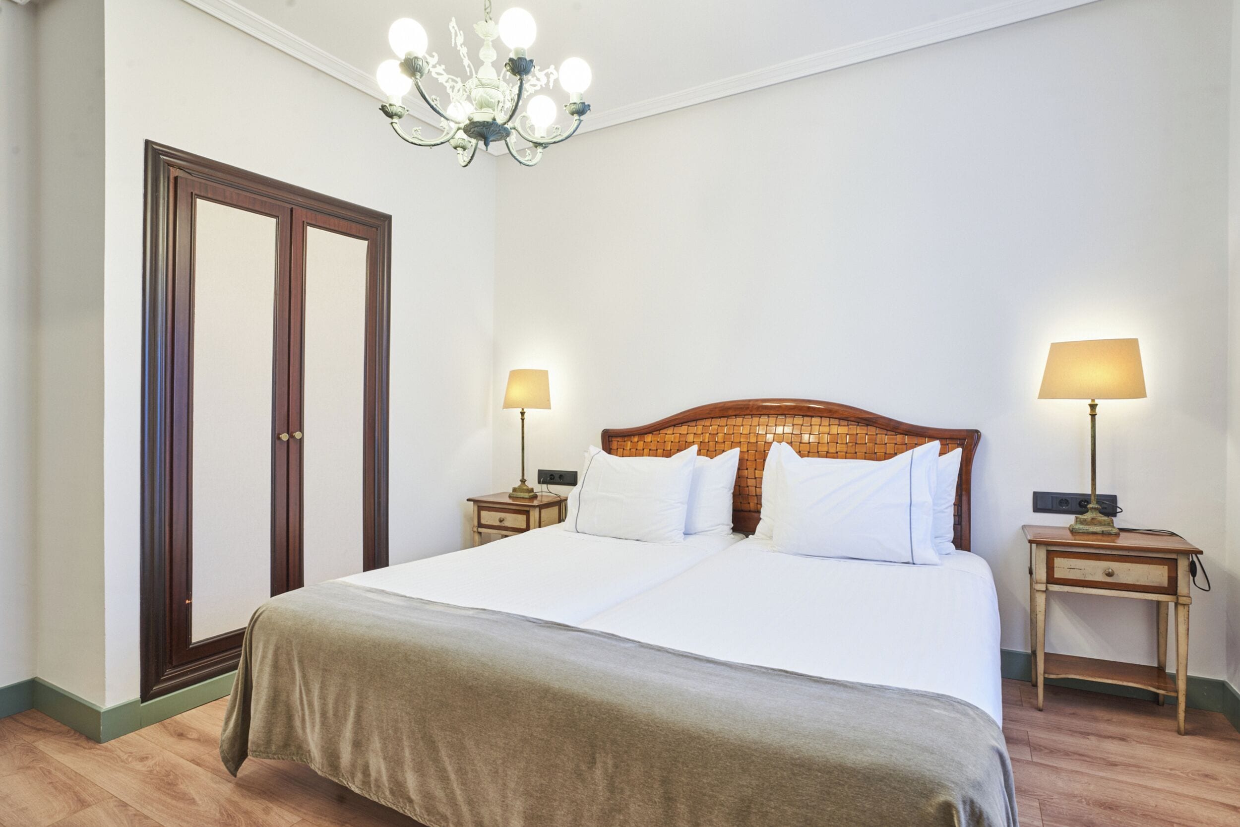 Une chambre d’hôtel avec un grand lit, deux tables de chevet avec des lampes, un lustre et une armoire en bois.