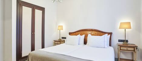 A hotel room with a large bed, two bedside tables with lamps, a chandelier, and a wooden wardrobe.