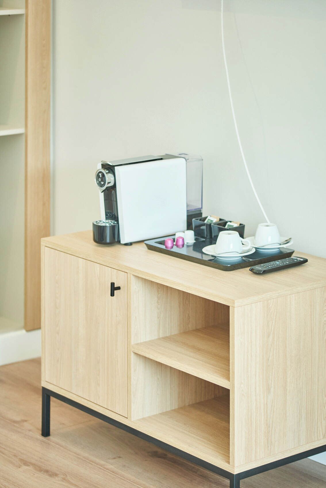 A wooden desk with a coffee machine, a remote control, and a cup.