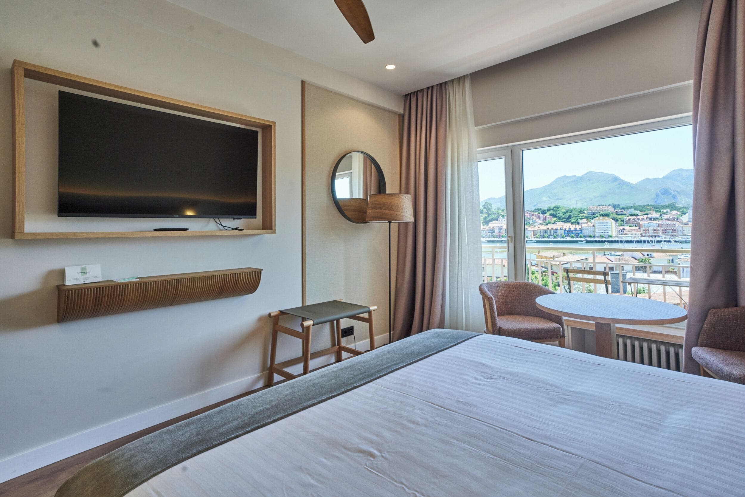 Habitación de hotel con cama, televisión, mesita, una silla y vistas a la ciudad y las montañas.