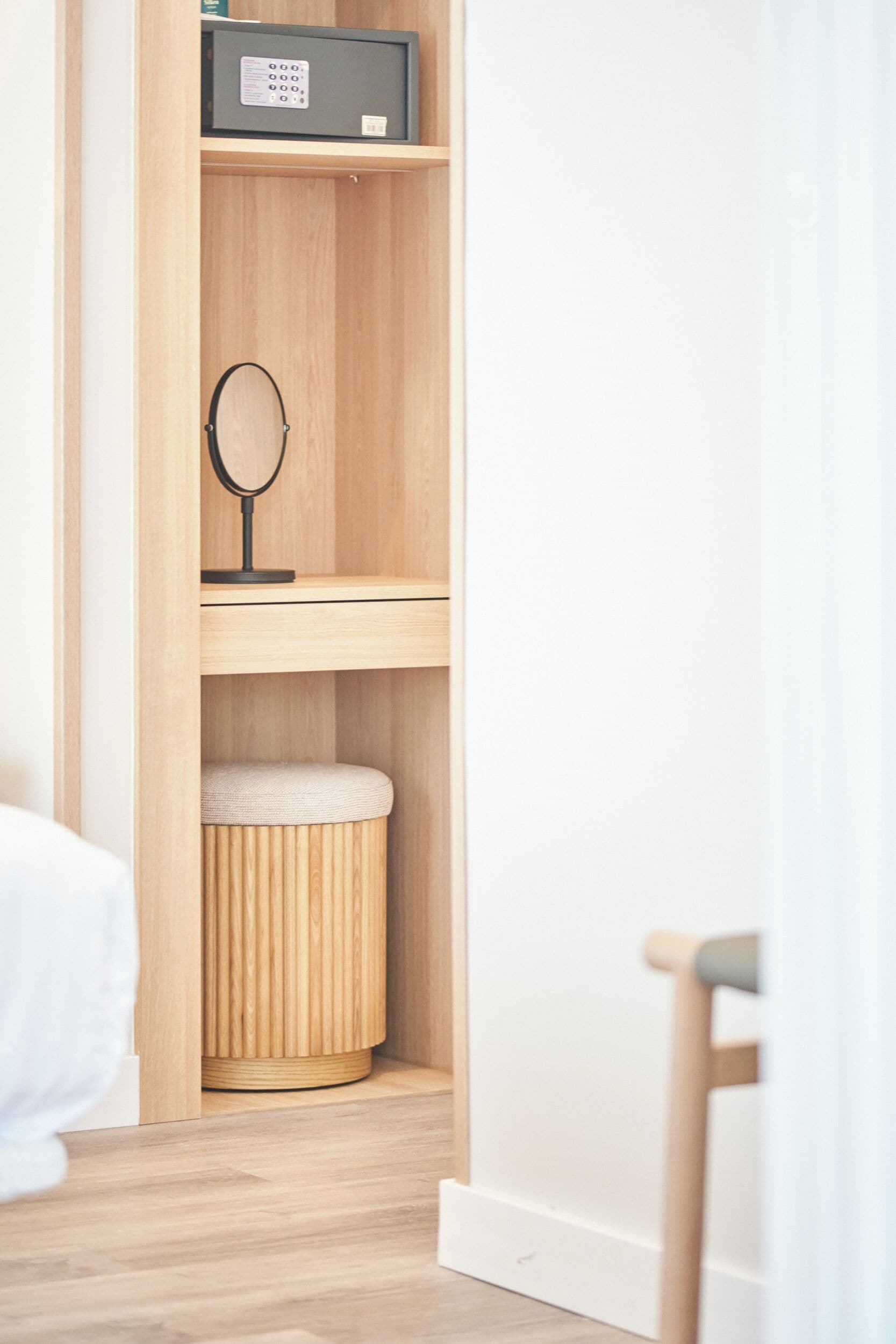 A wooden wardrobe with a mirror and a small stool inside.