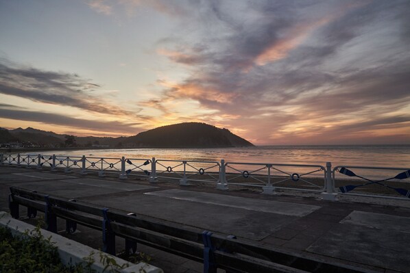 Un paseo marítimo con barandilla metálica, bancos y vista al mar al atardecer.