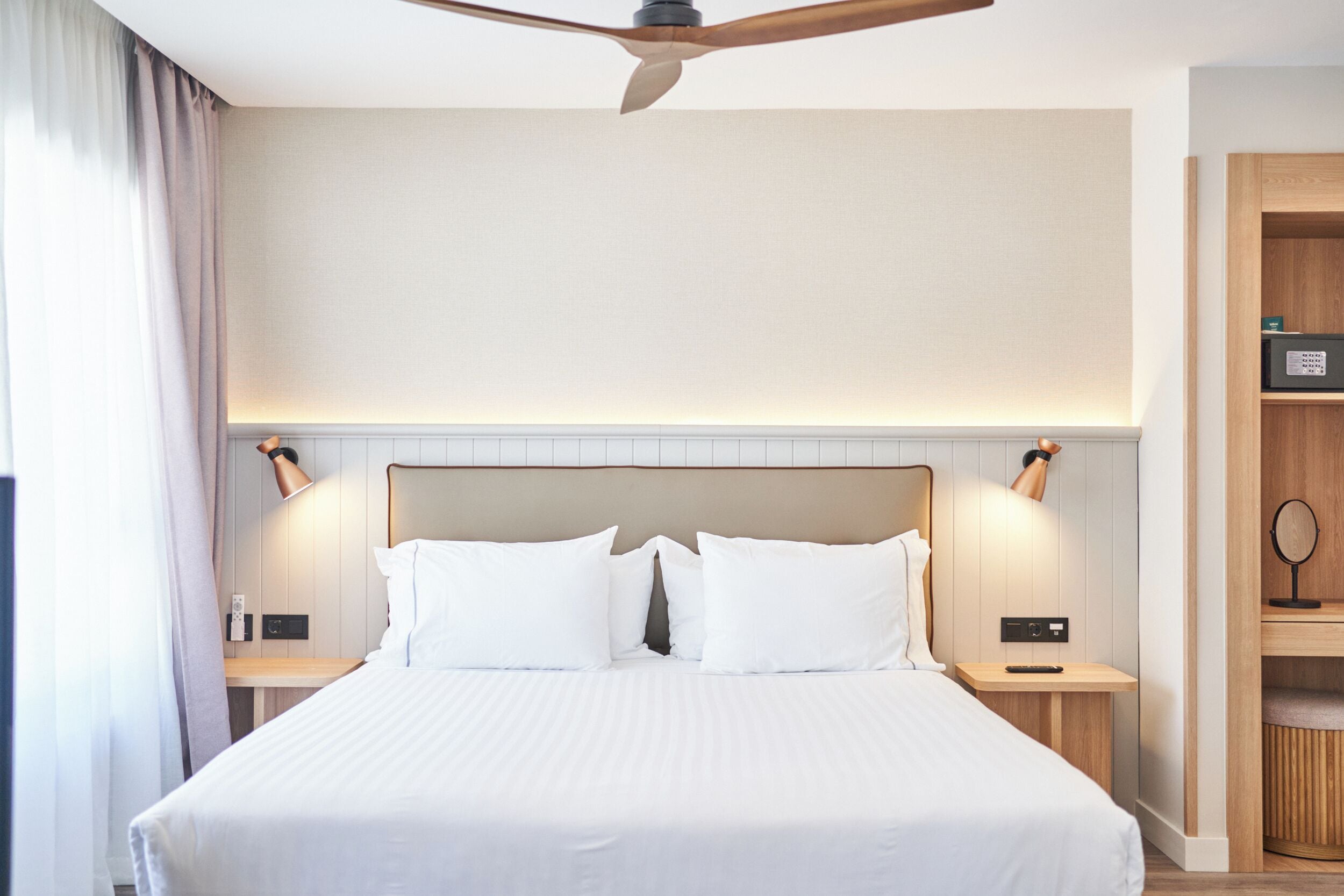 A hotel room with a large bed, two bedside tables, a ceiling fan, and a wooden nightstand with a mirror.