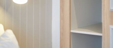 A room with a bed, a bedside table, a wall-mounted lamp, and a wooden shelf unit.