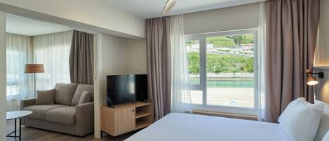 Ein Hotelzimmer mit Bett, Fernseher, Sofa, einem kleinen Tisch und einem Deckenventilator.