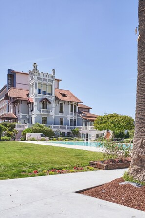 Un edificio grande de varios pisos con una torre destacada, una piscina y un césped bien cuidado.