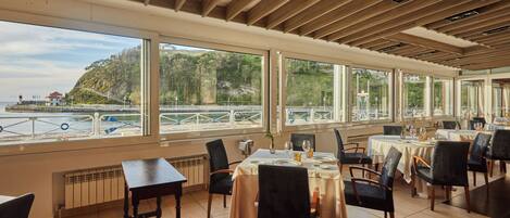 A restaurant with large windows offering a view of a coastal landscape.