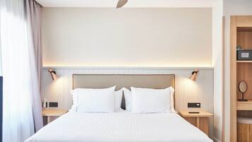 Habitación de hotel con una cama grande, lámparas de noche, ventilador de techo y un aparador de madera con espejo.