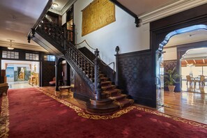 A grand staircase with ornate railings leading to an upper floor, a red carpeted area, and a large map on the wall. - Silken Gran Hotel del Sella (Ribadesella)
