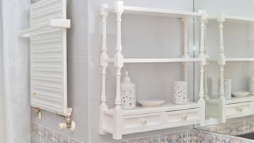 A bathroom with a white radiator, a white shelf with decorative items, and a tiled backsplash.