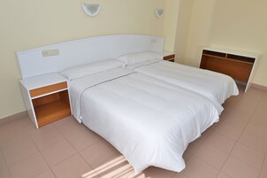Uma cama bem arrumada com roupa de cama branca, uma mesa de cabeceira de madeira e uma estante embutida.
