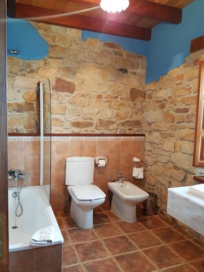 Ein Badezimmer mit Steinwand, Badewanne, Toilette und Bidet.
