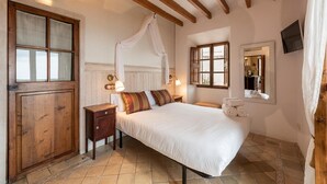 Une chambre à coucher avec un lit à baldaquin, des poutres en bois au plafond, une armoire en bois, une table de chevet avec des lampes et une fenêtre avec des rideaux.