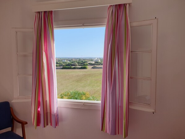 A room with a window featuring white shutters and colorful striped curtains. - Piscis (Ciutadella de Menorca)