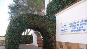 Un vialetto lastricato conduce a un edificio bianco con un cartello che indica un servizio di autonoleggio.