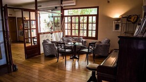 A room with a wooden floor, a round table with chairs, a piano, and large windows with a view of greenery. - Marbel (Cala Ratjada)