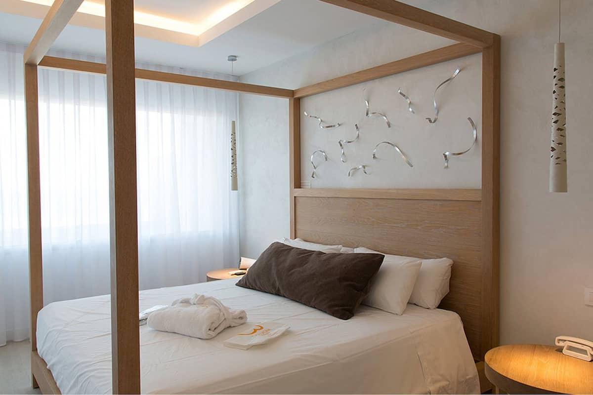 Une chambre d’hôtel moderne avec un lit à baldaquin, une tête de lit en bois et un élément décoratif mural.