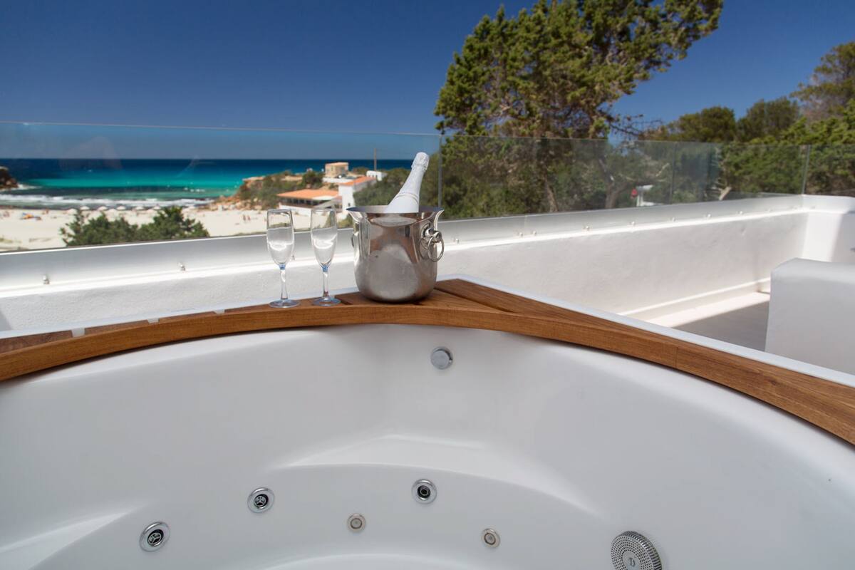 Un bain à remous bordé de bois, deux verres et une bouteille de champagne sur un balcon donnant sur une plage et l’océan.
