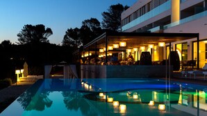 Un área de piscina al aire libre con un espacio de estar cubierto y un edificio al fondo.