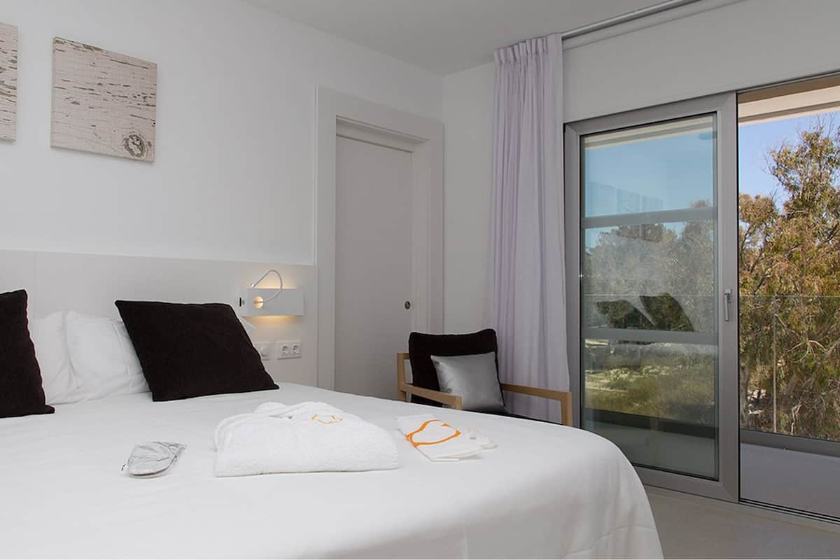 Une chambre d’hôtel avec un grand lit, un bureau et une vue sur les arbres par la fenêtre.