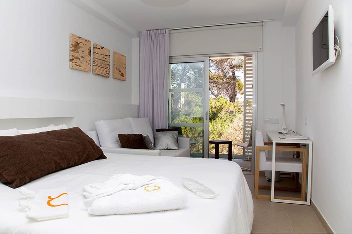 Une chambre d’hôtel moderne dotée d’un grand lit, d’un bureau et d’un balcon offrant une vue sur les arbres.