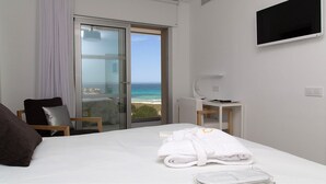Habitación de hotel con cama, escritorio, silla, televisor y vista al océano.