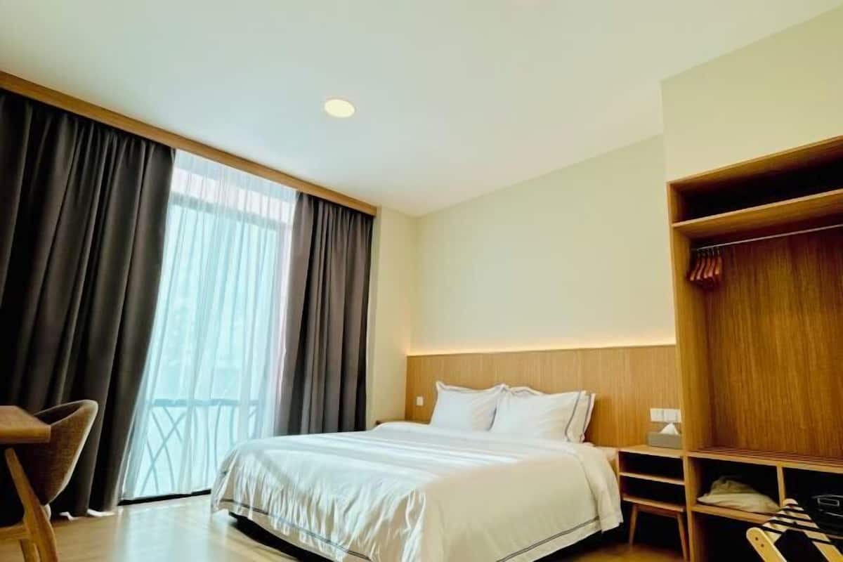A hotel room with a bed, a wooden wardrobe, a desk, and a chair.