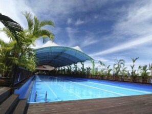 A swimming pool with a wooden deck, surrounded by palm trees and a large white tent-like structure.