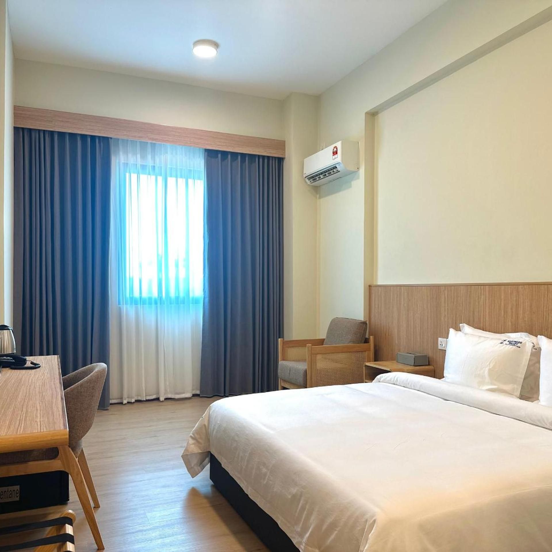 A hotel room with a bed, a desk, a chair, a nightstand, and a window with curtains.