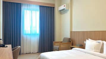 A hotel room with a bed, a desk, a chair, a nightstand, and a window with curtains.
