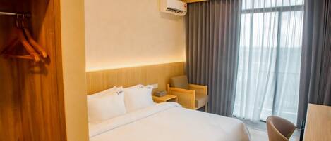 A hotel room with a bed, a desk, a chair, a wardrobe, and a window with curtains.