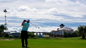 A person playing golf on a well-maintained green with a large house in the background. - Eastwood Valley Golf & Country Club (Miri)