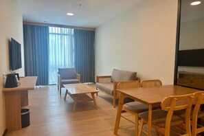 A hotel room with a wooden dining table, two sofas, a TV, and a window with curtains.
