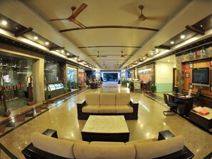 A hotel lobby with a central seating area, a reception desk, and a television screen.