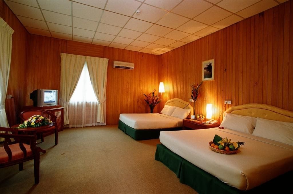 A hotel room with two beds, a desk, a television, and a window with curtains.