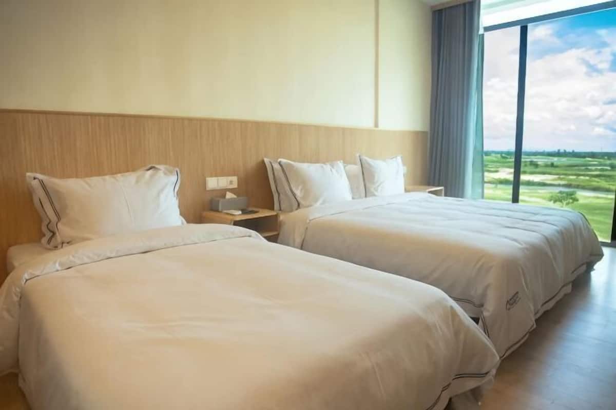A hotel room with two beds, a nightstand, and a large window with a view of the countryside.